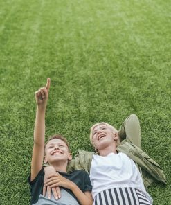 high angle view of happy mother and son looking up while lying together on green lawn